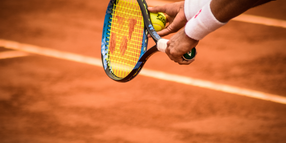 A tennis racket and tennis ball being used on a clay court